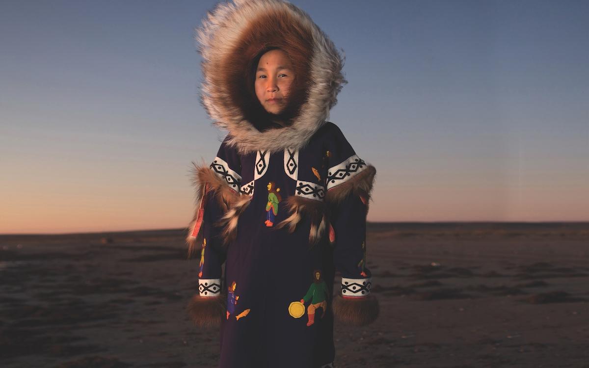 CARMELLA KLENGENBERG WEARS HER GRANDMOTHER’S DRUM-DANCING PARKA, MADE FROM STROUD, WITH WOLVERINE TRIM AND A WOLF SUNBURST PATTERN LINING THE HOOD. THE RED DYE ON THE UNDERSIDE OF THE FRINGES WAS BELIEVED TO BRING GOOD LUCK AND IS A DETAIL STILL SEEN ON PARKAS TODAY. 