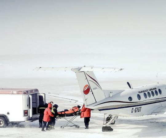 Nunavut Lifeline: Medics rush a patient in Arviat onto a King Air 200 for a medevac to Manitoba before a winter storm hits. Photo by Paul Aningat. 