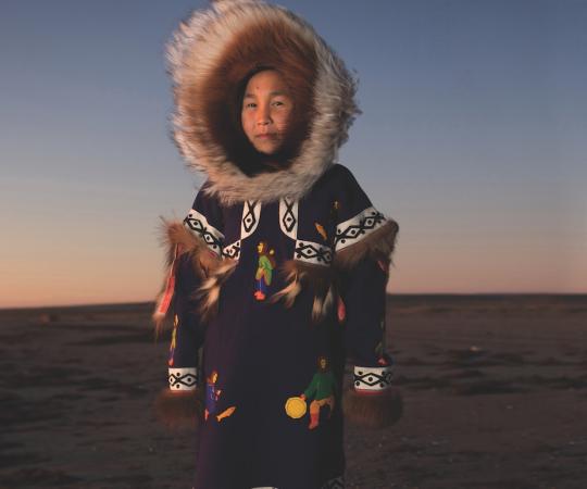CARMELLA KLENGENBERG WEARS HER GRANDMOTHER’S DRUM-DANCING PARKA, MADE FROM STROUD, WITH WOLVERINE TRIM AND A WOLF SUNBURST PATTERN LINING THE HOOD. THE RED DYE ON THE UNDERSIDE OF THE FRINGES WAS BELIEVED TO BRING GOOD LUCK AND IS A DETAIL STILL SEEN ON PARKAS TODAY. 