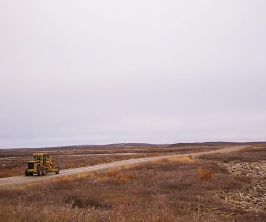Pingos dot the landscape along the road winding south out of Tuktoyaktuk. Ryan Yakeleya, an E. Gruben's employee, drives a grader toward the Tuk-Inuvik highway worksite. Photo by Angela Gzowski